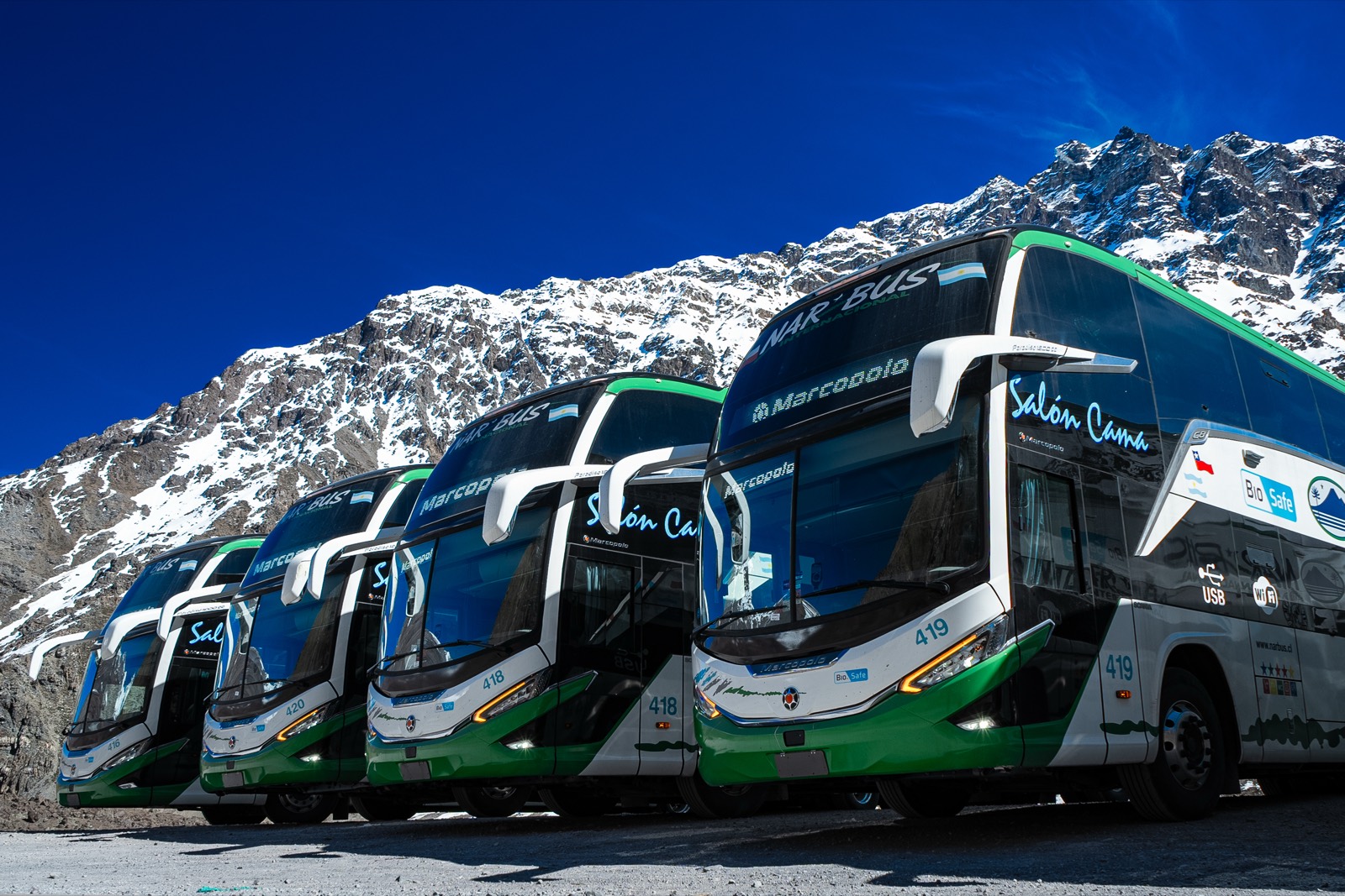 Buses Salón Cama de Nar Bus Internacional estacionados frente a la cordillera nevada